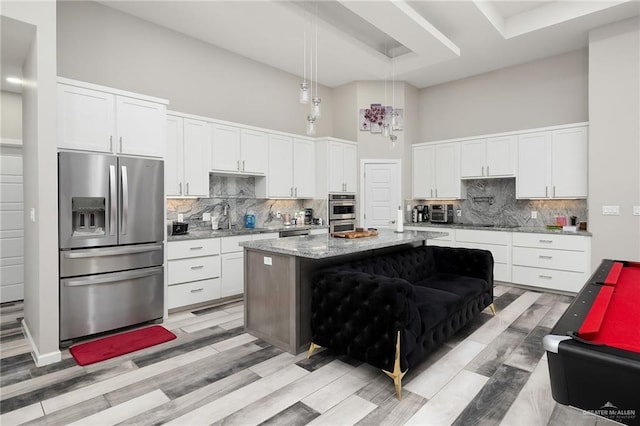 kitchen featuring appliances with stainless steel finishes, light wood-style flooring, a towering ceiling, and decorative backsplash