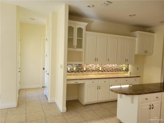 kitchen with backsplash, dark stone countertops, white cabinetry, and light tile patterned floors