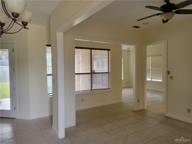 empty room with light tile patterned floors, ceiling fan with notable chandelier, and a healthy amount of sunlight