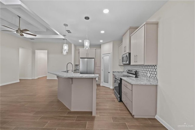 kitchen with a center island with sink, sink, hanging light fixtures, light stone countertops, and stainless steel appliances