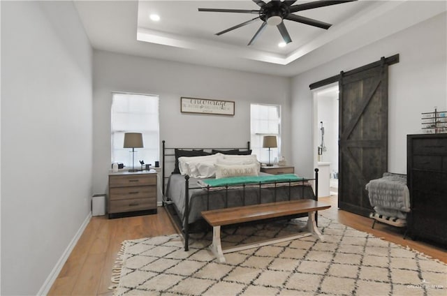 bedroom with ceiling fan, a barn door, a raised ceiling, and light wood-type flooring