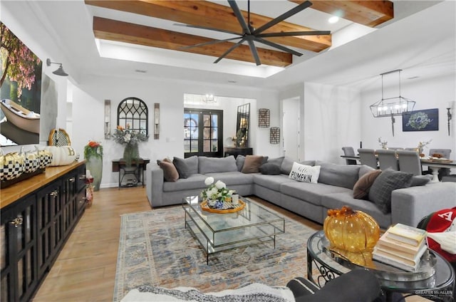 living room featuring beam ceiling, light hardwood / wood-style floors, and ceiling fan with notable chandelier