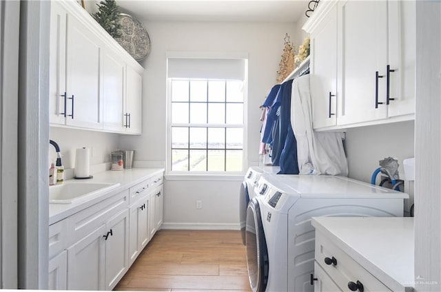 clothes washing area with cabinets, light hardwood / wood-style floors, separate washer and dryer, and sink