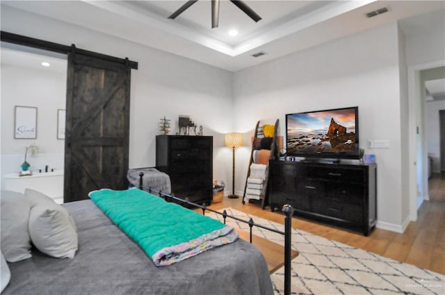 bedroom featuring hardwood / wood-style flooring, ceiling fan, a barn door, and a tray ceiling