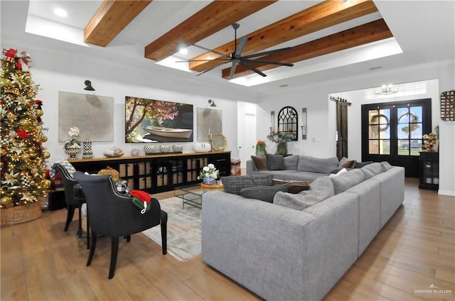 living room with ceiling fan with notable chandelier, light hardwood / wood-style floors, beam ceiling, and french doors