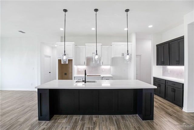 kitchen featuring light countertops, decorative backsplash, white cabinets, a sink, and a kitchen island with sink