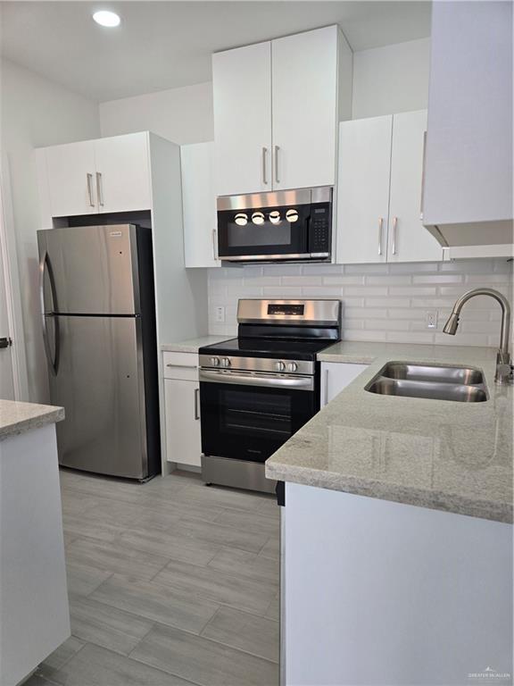 kitchen with white cabinets, light stone countertops, stainless steel appliances, and a sink