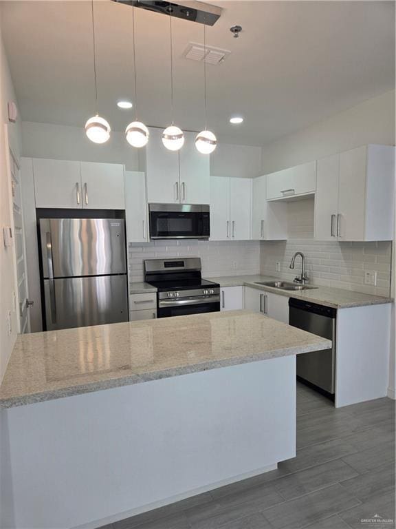 kitchen with light stone counters, a sink, stainless steel appliances, a peninsula, and white cabinetry