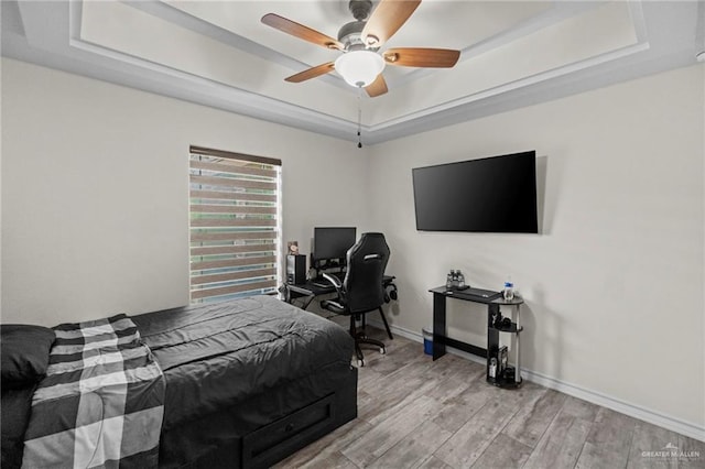 bedroom with ceiling fan, a raised ceiling, and light hardwood / wood-style flooring