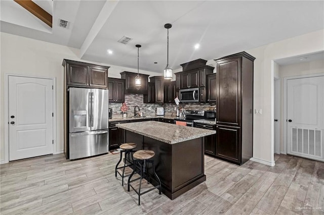 kitchen featuring a center island, light stone counters, backsplash, pendant lighting, and appliances with stainless steel finishes