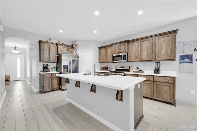 kitchen with appliances with stainless steel finishes, an island with sink, sink, a breakfast bar area, and light hardwood / wood-style flooring