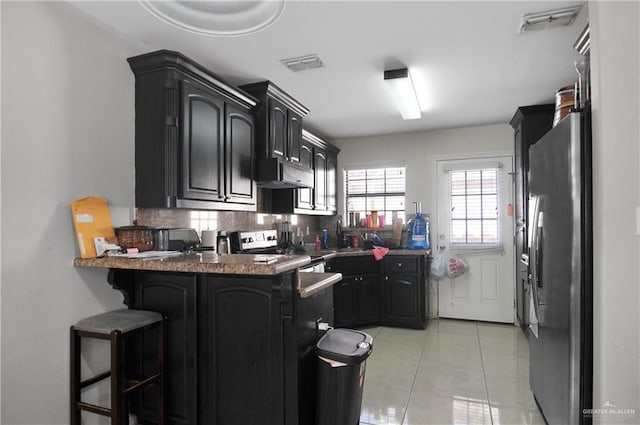 kitchen with kitchen peninsula, appliances with stainless steel finishes, backsplash, a kitchen breakfast bar, and light tile patterned flooring