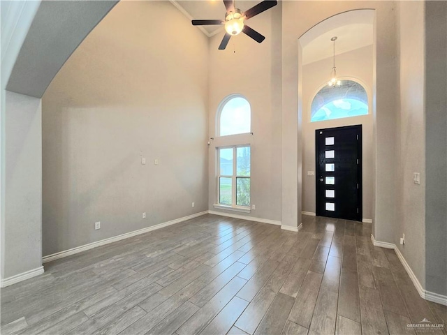 foyer with a towering ceiling, a ceiling fan, baseboards, and wood finished floors