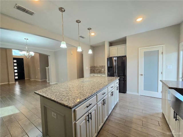 kitchen featuring wood finish floors, a center island, visible vents, hanging light fixtures, and refrigerator with ice dispenser