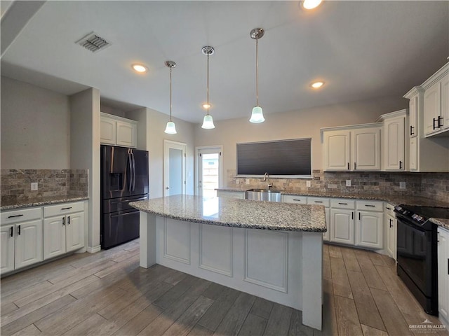 kitchen with visible vents, a kitchen island, wood finish floors, black appliances, and a sink