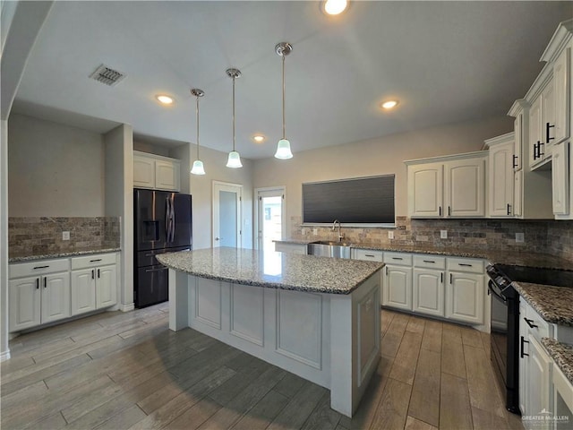 kitchen with light wood-style flooring, white cabinetry, visible vents, a center island, and black appliances