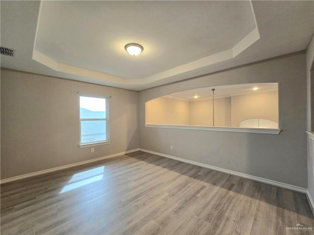 empty room with baseboards, visible vents, a raised ceiling, and wood finished floors