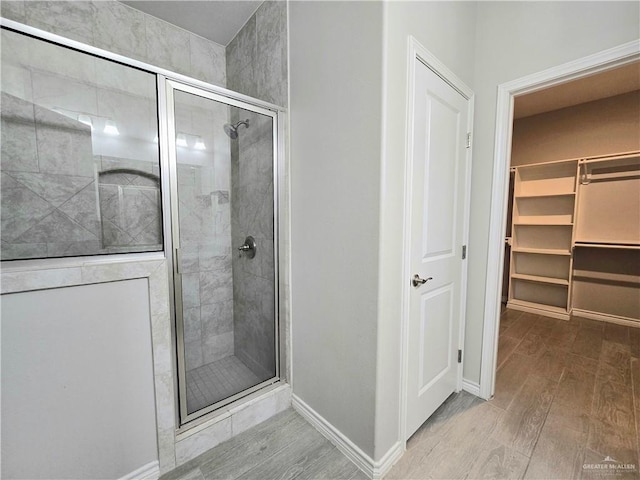 full bathroom featuring a walk in closet, a shower stall, baseboards, and wood finished floors