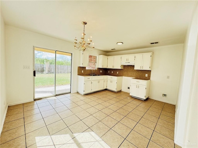 kitchen featuring white cabinetry, backsplash, a chandelier, decorative light fixtures, and light tile patterned flooring