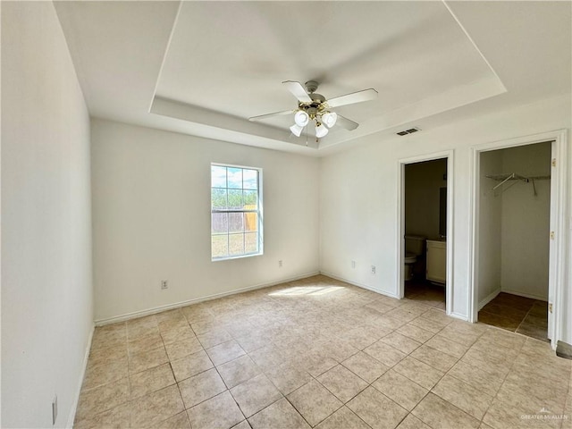 unfurnished bedroom with ensuite bath, a spacious closet, ceiling fan, a raised ceiling, and a closet