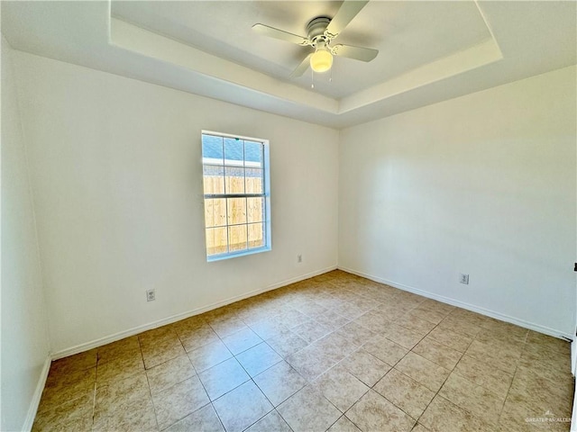 tiled empty room with a raised ceiling and ceiling fan