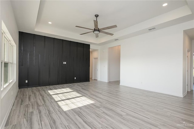 unfurnished room featuring a tray ceiling, light wood-style floors, a ceiling fan, and visible vents