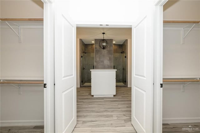 full bath with a spacious closet, a shower stall, an inviting chandelier, and wood finished floors