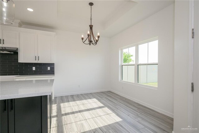 kitchen featuring light wood-style floors, white cabinets, under cabinet range hood, decorative backsplash, and a notable chandelier