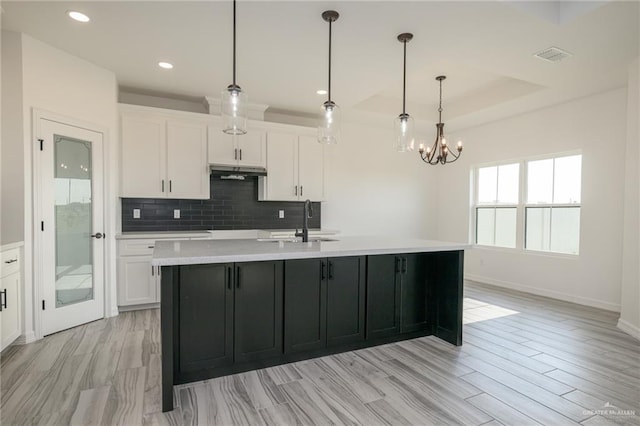 kitchen with white cabinets, under cabinet range hood, light countertops, and baseboards