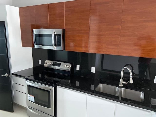 kitchen featuring dark stone counters, white cabinets, sink, tasteful backsplash, and stainless steel appliances