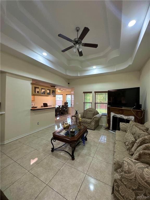 living room with light tile patterned floors, ceiling fan, recessed lighting, and a tray ceiling