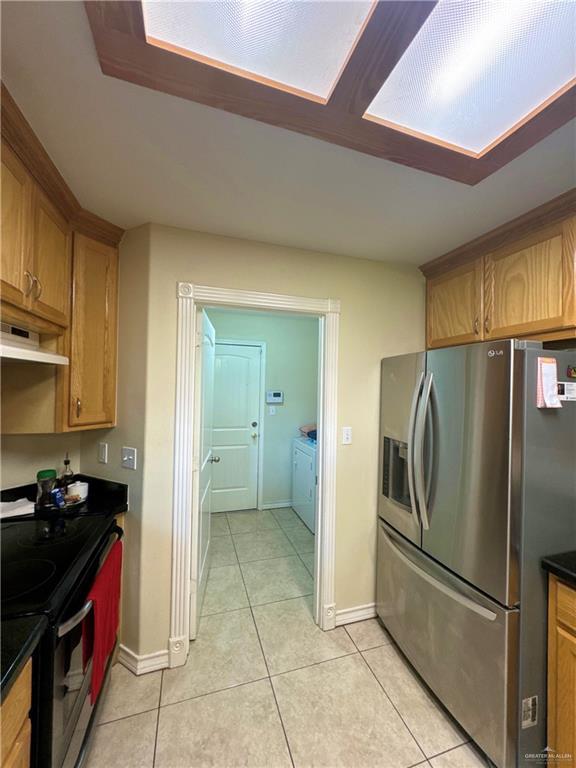 kitchen featuring light tile patterned floors, appliances with stainless steel finishes, under cabinet range hood, dark countertops, and baseboards