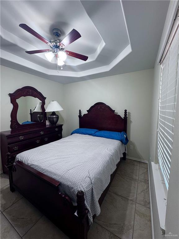 bedroom featuring a raised ceiling, ceiling fan, marble finish floor, and baseboards