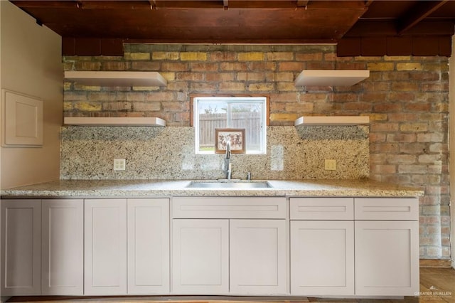 kitchen featuring light stone counters, sink, backsplash, and white cabinets