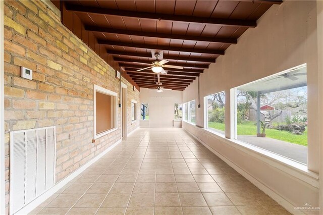 unfurnished room with beamed ceiling, brick wall, a healthy amount of sunlight, and wood ceiling