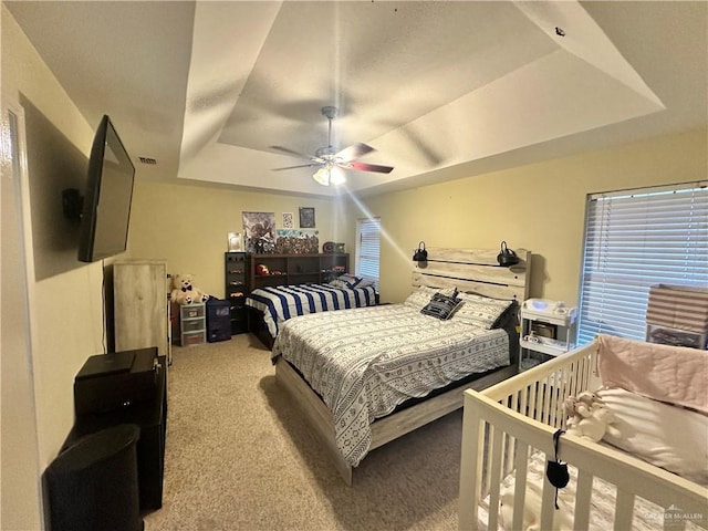 bedroom with ceiling fan, light colored carpet, and a tray ceiling