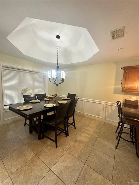 tiled dining area featuring a chandelier and a raised ceiling