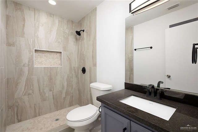 bathroom featuring a tile shower, vanity, and toilet