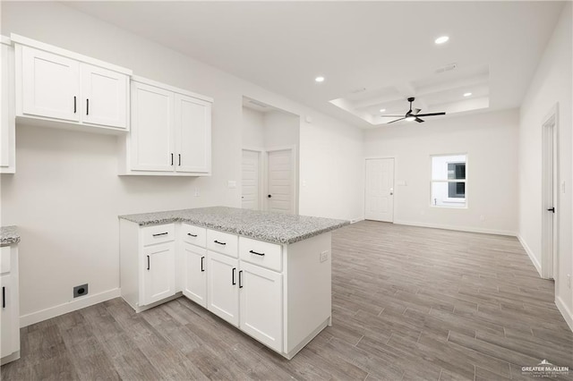 kitchen with light stone countertops, white cabinetry, light wood-type flooring, a raised ceiling, and kitchen peninsula