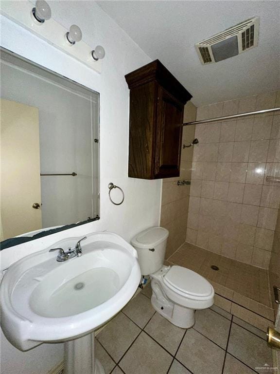 bathroom with tile patterned flooring, toilet, and a tile shower