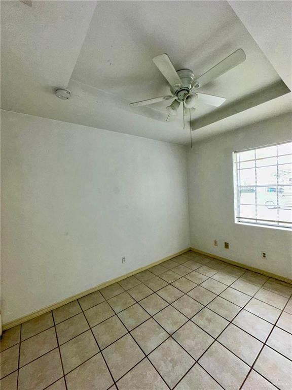 spare room with ceiling fan, light tile patterned flooring, and a tray ceiling