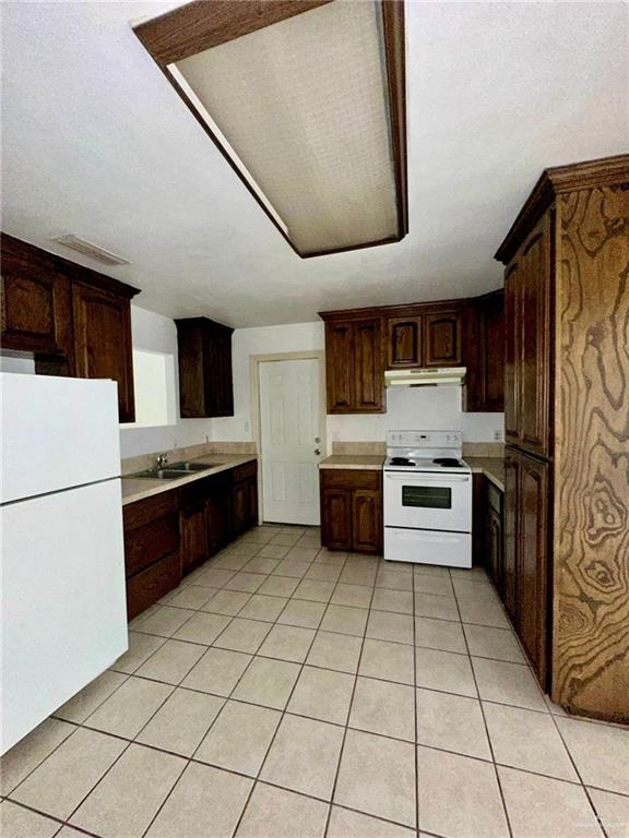 kitchen with dark brown cabinets, light tile patterned flooring, white appliances, and sink