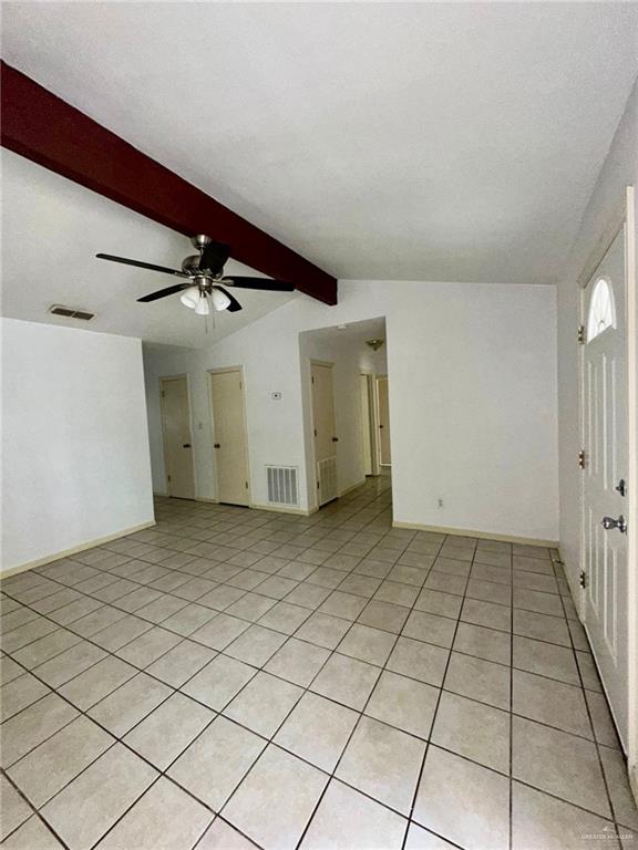 tiled spare room featuring ceiling fan and lofted ceiling with beams