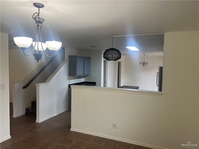 interior space with kitchen peninsula, dark tile patterned floors, an inviting chandelier, stainless steel refrigerator, and hanging light fixtures