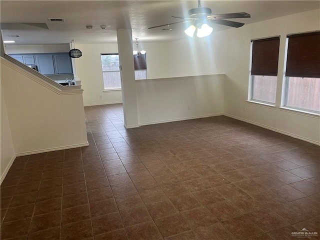 empty room with dark tile patterned flooring and ceiling fan with notable chandelier