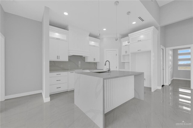 kitchen with baseboards, a sink, white cabinetry, and an island with sink