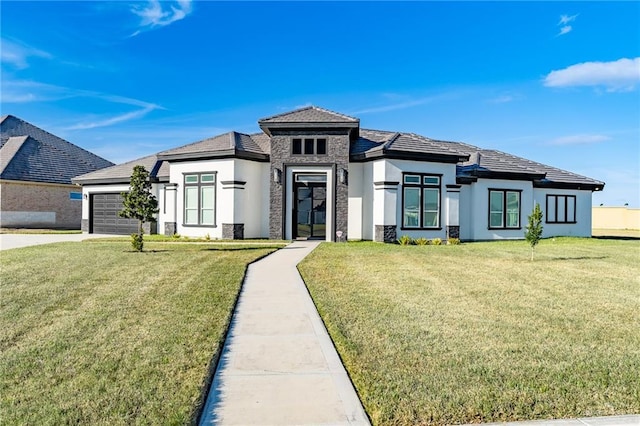 prairie-style home with stucco siding, a garage, stone siding, driveway, and a front lawn