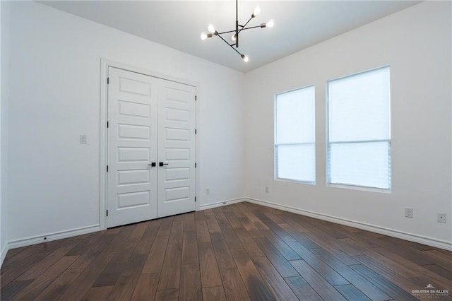 spare room with dark wood-style floors, baseboards, and a chandelier