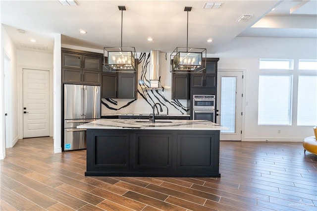 kitchen featuring stainless steel appliances, visible vents, a center island with sink, and decorative light fixtures