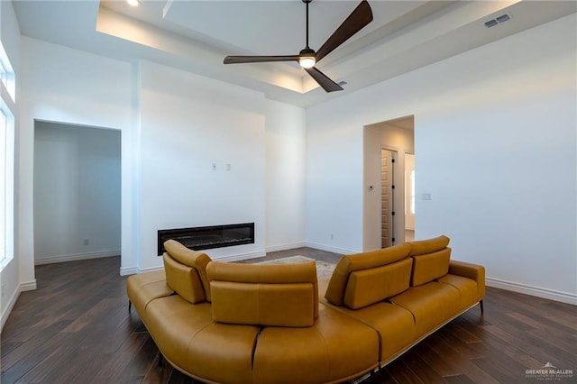 living area featuring a tray ceiling, dark wood finished floors, and a glass covered fireplace